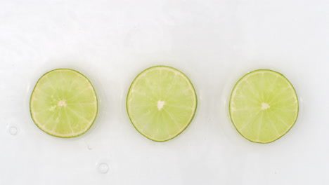 Water-splashes-in-slow-motion.-Top-view:-three-slices-of-green-lime-washed-by-water-on-a-white-background